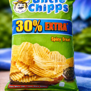Green pack of Uncle Chipps Spicy Treat potato chips with “30% Extra” offer printed on the front, placed on a blue floral background.